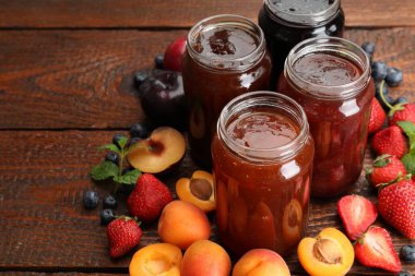 Kavanozlardaki farklı reçeller ve ahşap masadaki malzemeler, yakın plan.