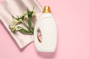 Bir şişe yumuşatıcı, çiçekler ve pembe arka planda bej kumaş, düz bir zemin.