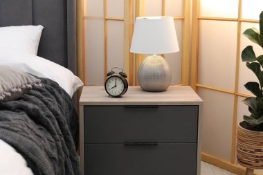 İçeride yatağın yanında çalar saat ve lamba olan komodinin yanında.