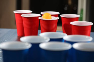 Bira pong oyunu. İçkili plastik bardaklar ve masada top, yakın plan.