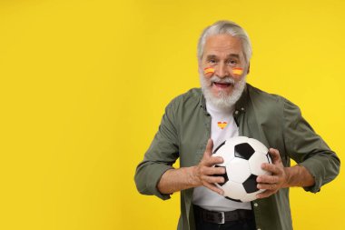 Yüzünde İspanya bayrağı ve futbol topunu sarı arka planda tutan tişörtle uyumlu renkte vantilatör. Metin için boşluk