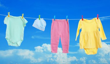 Mavi gökyüzüne karşı çamaşır ipinde kurumuş farklı bebek kıyafetleri.
