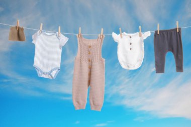 Mavi gökyüzüne karşı çamaşır ipinde kurumuş farklı bebek kıyafetleri.
