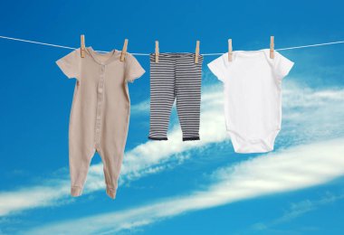 Mavi gökyüzüne karşı çamaşır ipinde kurumuş farklı bebek kıyafetleri.