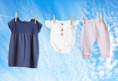 Mavi gökyüzüne karşı çamaşır ipinde kurumuş farklı bebek kıyafetleri.