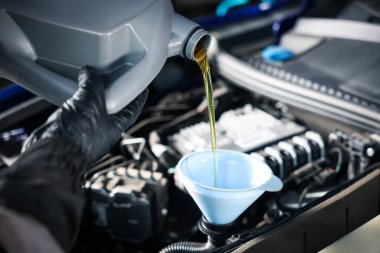 İşçi motor yağını teneke kutudan araba motoruna boşaltıyor.