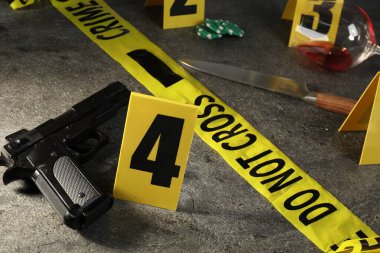 Adli tıp uzmanı. Sarı olay yeri bandı, işaretler ve kanıtlar gri masada, yakın plan.