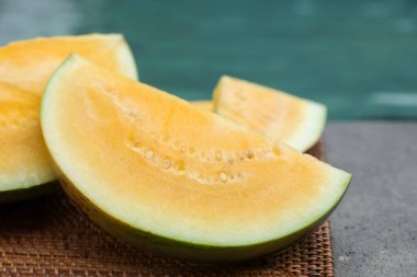 Olgun sarı karpuz parçaları hasır masada, yüzme havuzunun yanında, yakın plan.