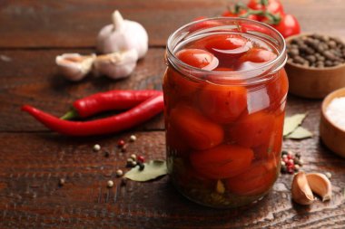 Kavanozda salamura domates ve ahşap masada malzemeler, yakın plan.