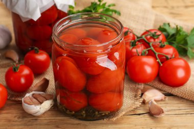 Kavanozda lezzetli domates turşusu, taze olanlar ve ahşap masada sarımsak, yakın plan.