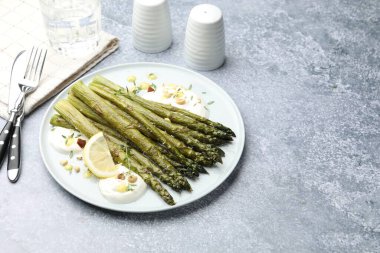 Lezzetli pişmiş kuşkonmaz, limon ve sosla servis ediliyor gri masada, yazı için yer var.