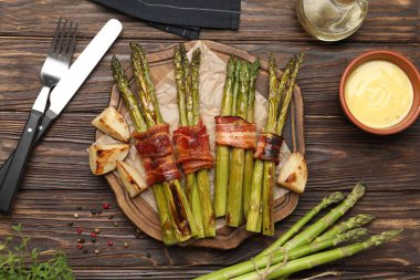 Lezzetli pişmiş kuşkonmaz, domuz pastırması ve ahşap masada sos ile servis edilir.