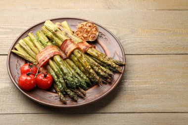 Ahşap masada domuz pastırması ve baharatla servis edilen lezzetli pişmiş kuşkonmaz, yakın plan. Metin için boşluk
