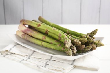 Beyaz ahşap masada taze çiğ kuşkonmaz mızrakları, yakın plan.