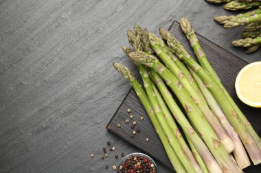 Taze çiğ kuşkonmaz mızrakları, limon ve baharatlar siyah masada, düz yerde. Metin için boşluk