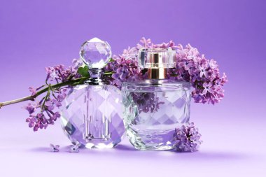 Parfüm şişeleri ve mor arkaplanda leylak çiçekleri olan dallar, yakın plan.