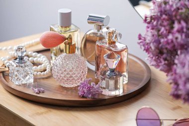 Parfüm şişeleri, aksesuarlar ve ahşap masada leylak çiçekleri.