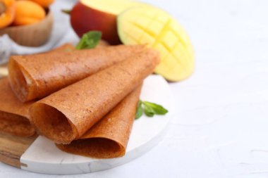 Lezzetli meyve dürümleri, nane, mango ve kayısılar beyaz masada, yakın plan. Metin için boşluk