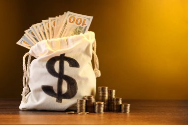 Dolar banknotları ve ahşap masaya istiflenmiş bozuk paralarla dolu çanta, sarı eğimli arkaplan, metin için boşluk