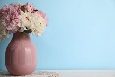 Açık mavi duvarın yanındaki beyaz masada vazodaki güzel şakayıklar. Metin için boşluk