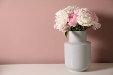 Pembe duvarın yanındaki beyaz masada vazodaki güzel şakayıklar. Metin için boşluk