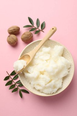 Doğal Shea yağı, fındık ve yapraklar pembe arka planda, düz yatıyordu.