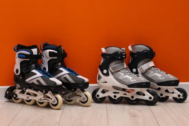 Turuncu duvarın yanında yerde çift patenler var.