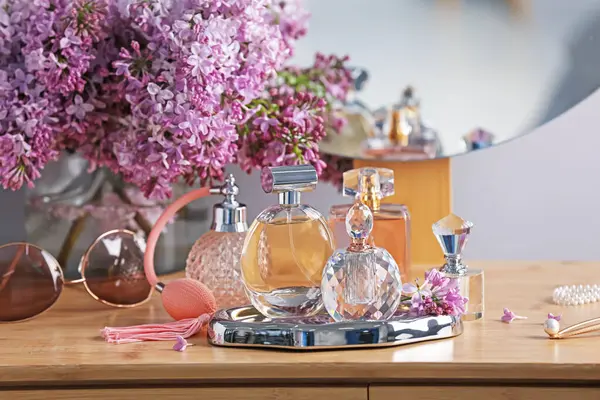 Parfüm şişeleri, aksesuarlar ve ahşap masada leylak çiçekleri.