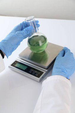 Bilim adamı beyaz masadaki terazide numune tartıyor, yakın plan.