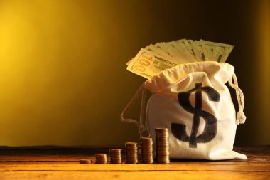 Dolar banknotları ve ahşap masaya istiflenmiş bozuk paralarla dolu çanta, sarı eğimli arkaplan, metin için boşluk