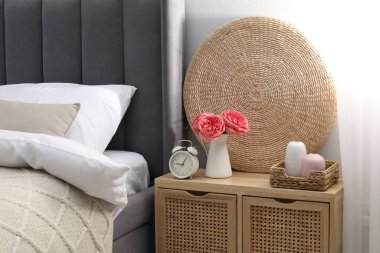 Yatağın yanında alarm saati ve dekorasyonu olan komodinin yanında.