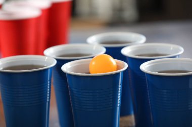 Bira pong oyunu. İçkili plastik bardaklar ve masada top, yakın plan.