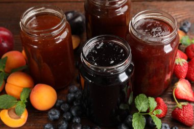 Kavanozlardaki farklı reçeller ve ahşap masadaki malzemeler, yakın plan.