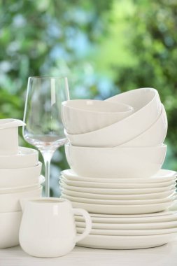 Beyaz masadaki farklı temiz tabaklar, bulanık yeşil arka plan, yakın plan