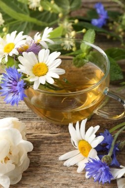 Cam bardakta Aromatik bitki çayı, tahta masada çiçekler ve yeşil yapraklar, yakın plan.