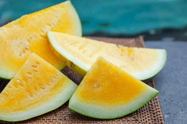 Olgun sarı karpuz parçaları hasır masada, yüzme havuzunun yanında, yakın plan.