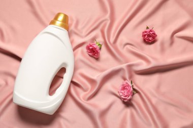 Bir şişe yumuşatıcı ve pembe kumaş üzerinde çiçekler.