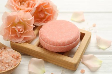 Sabun çubuğu, deniz tuzu ve beyaz ahşap masada güzel çiçekler, yakın plan.