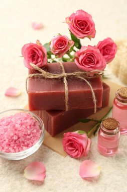 Sabun çubukları, deniz tuzu, temel yağlar ve bej masadaki güzel güller, yakın plan.