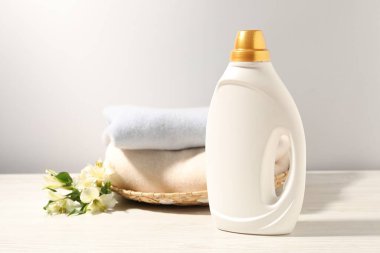 Bir şişe yumuşatıcı, temiz kıyafetler ve beyaz ahşap masa üzerinde zambak çiçekleri.