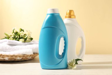 Beyaz ahşap masada açık sarı arka plana karşı yumuşatıcı, terry havlu ve zambak çiçekleri.