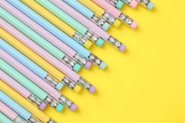 Sarı arka planda silgisi olan bir sürü grafit kalem, düz bir zemin. Metin için boşluk