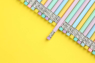 Sarı arka planda silgisi olan bir sürü grafit kalem, düz bir zemin. Metin için boşluk