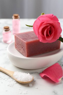 Sabun barları, kozmetik ürünleri ve beyaz mermer masada güzel bir gül.