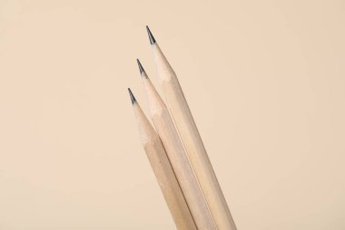 Bej arka planda üç grafit kalem, yakın plan.