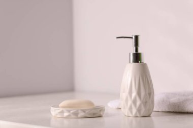 Sabun çubuğu, bir şişe kozmetik ürünü ve beyaz masada havlu.