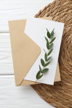 Boş davetiye kartı, zarf, dal ve hasır paspas beyaz ahşap masa, üst görünüm