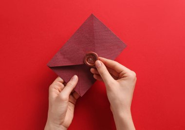 Kırmızı arka planda balmumu mühürü olan güzel bir davetiye zarfı tutan kadın.