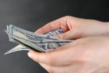 Gri arka planda dolar banknotları sayan kadın, yakın plan.