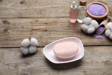 Sabun çubuğu, kozmetik ürünleri ve pamuk çiçekleri ahşap masanın üstünde.